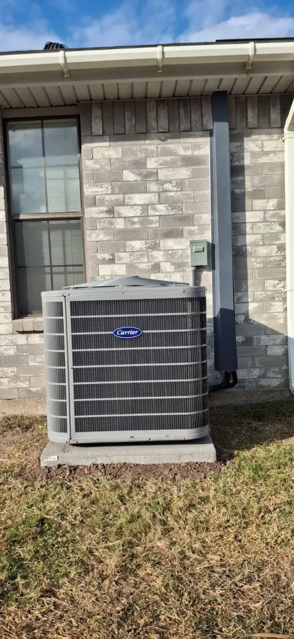 Carrier outdoor AC unit set level on a concrete pad next to a gray brick house